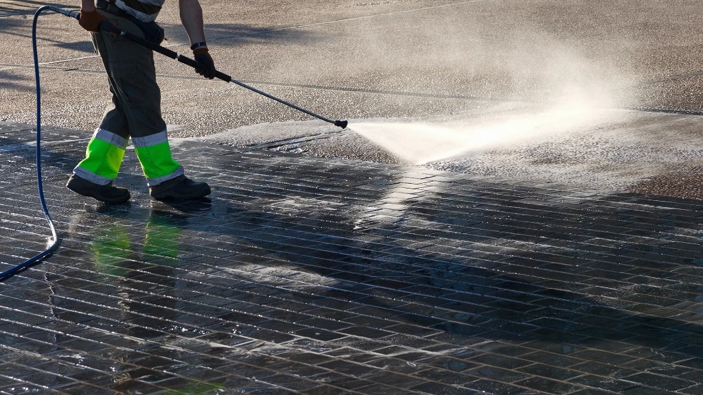 Operator pressure washing exterior paving with professional cleaning equipment